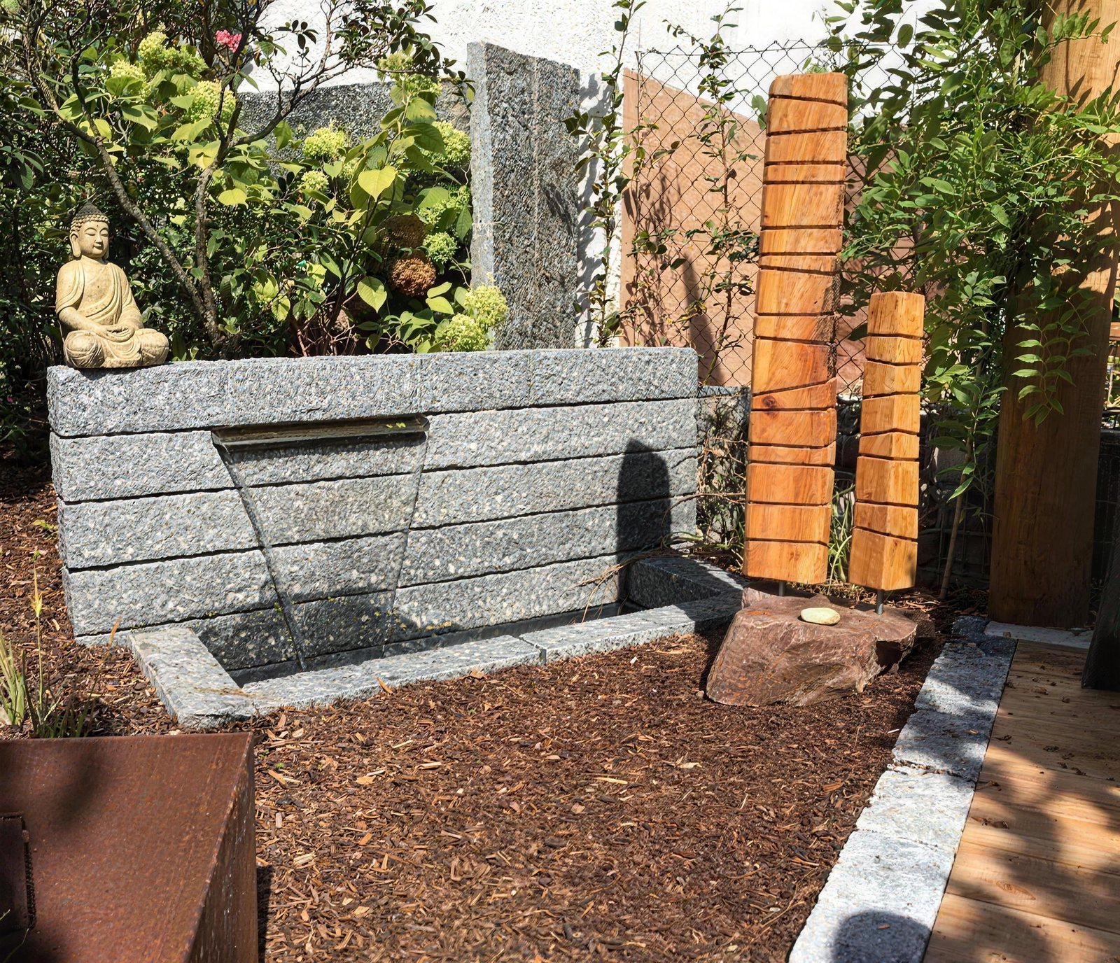 Granit-Zierbrunnen mit Wasserlauf in einem Beet mit Rindenmulch