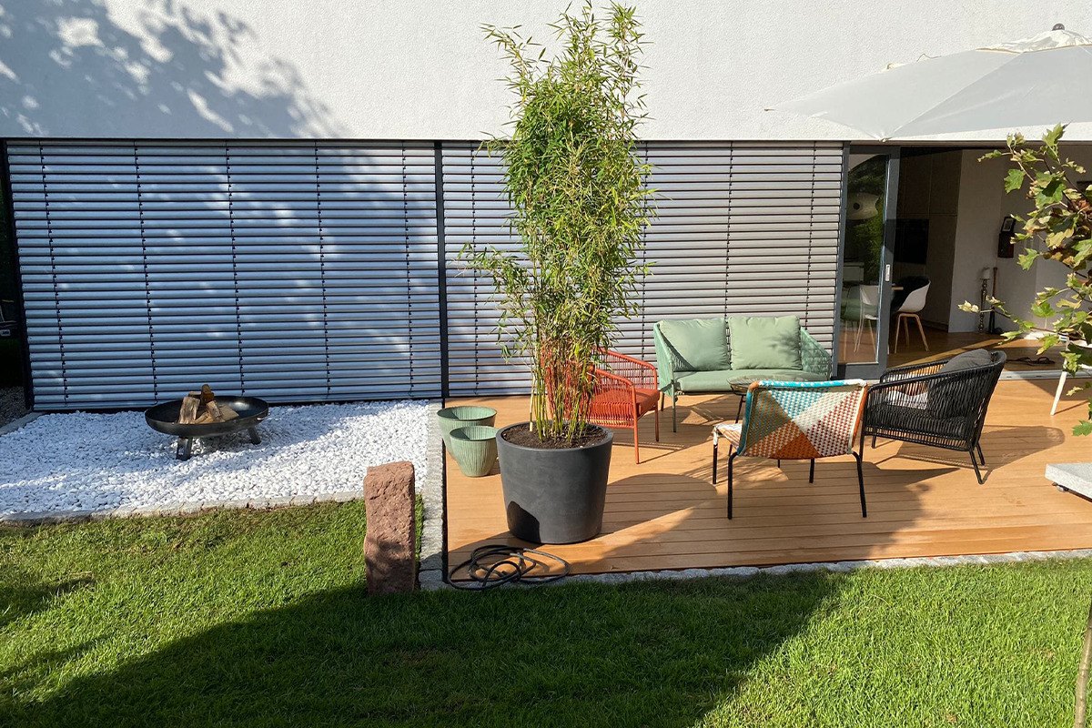 Holzterrasse mit Sitzgruppe und Rollrasen an einem modernen Wohnhaus