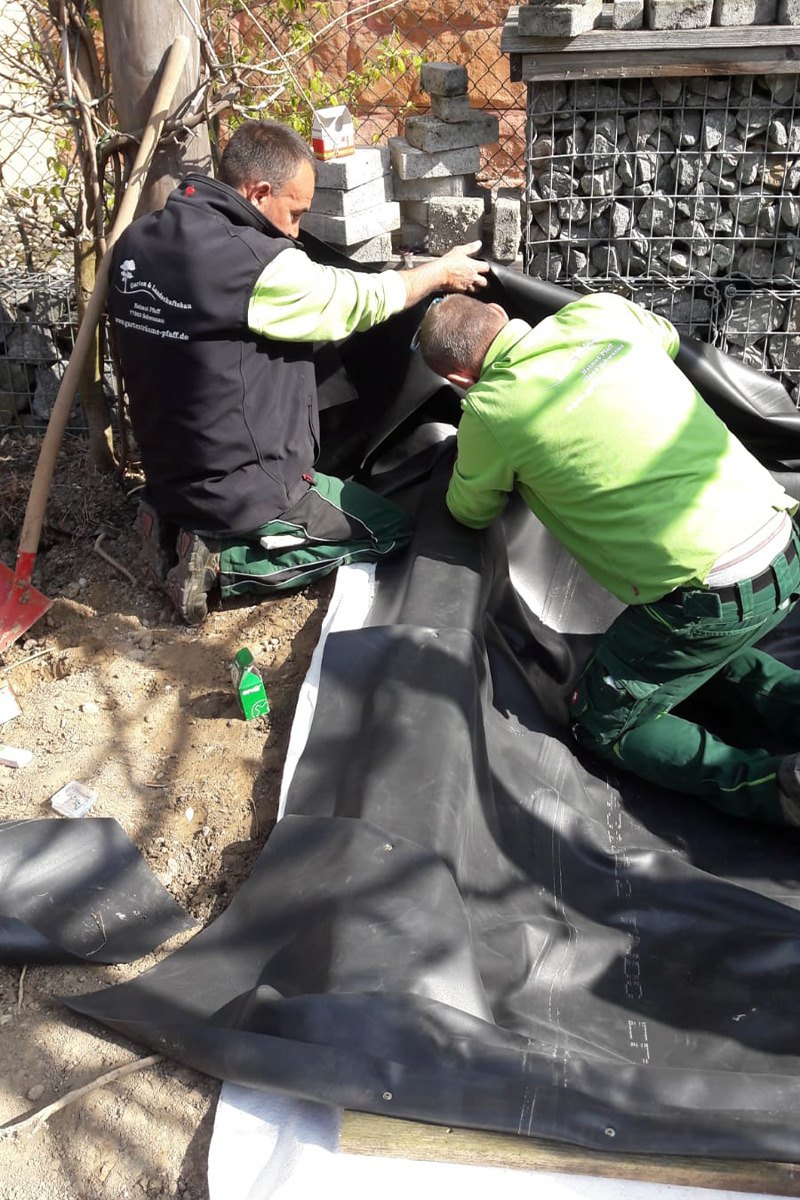 Zwei Mitarbeiter verlegen Teichfolie beim Bau eines Hundepools